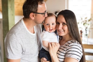 Beautiful young parents at home holding their cute baby son in the arms.