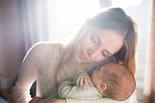 Beautiful young mother holding her sleeping baby son in her arms, eyes closed