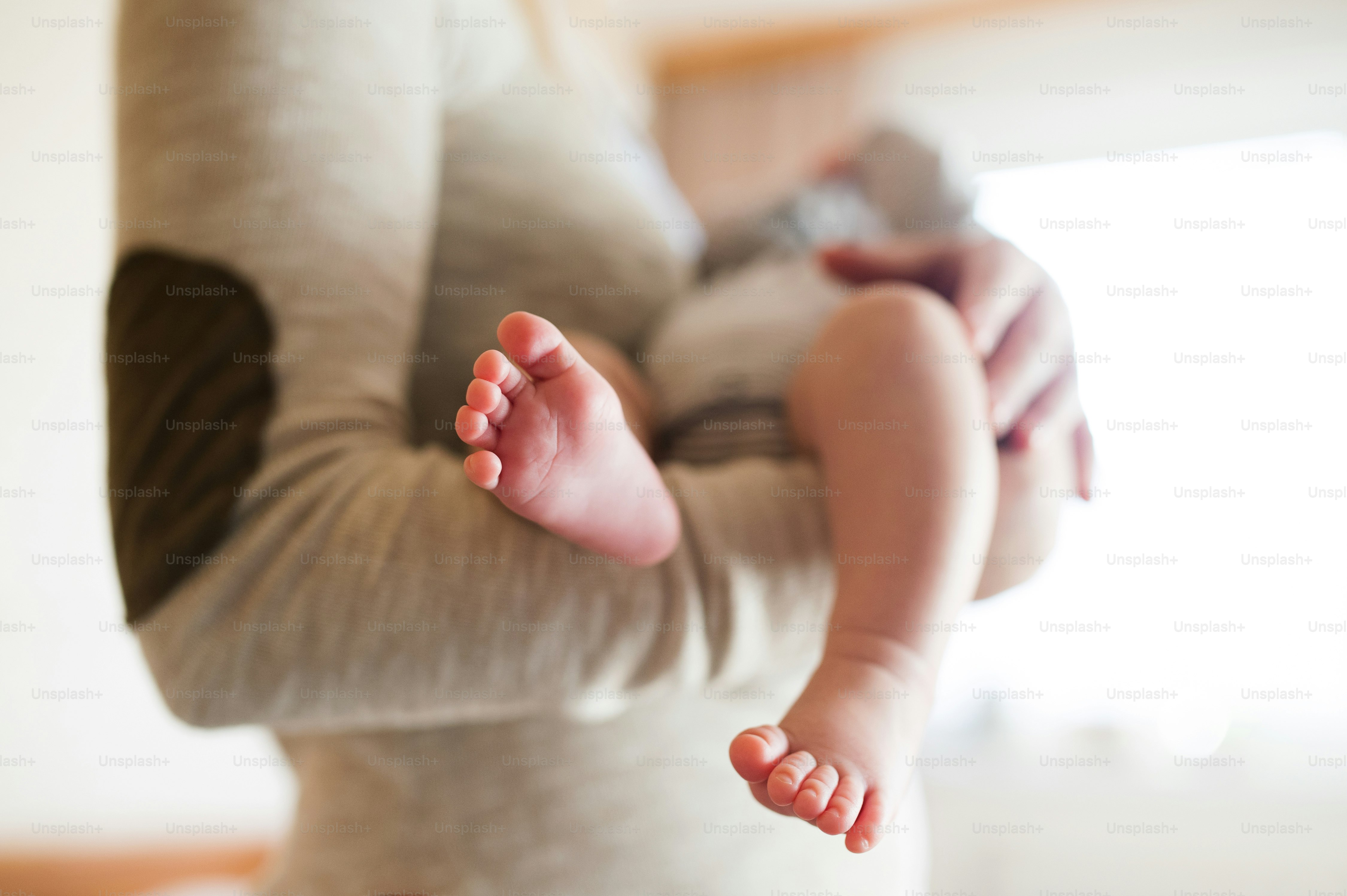 Ibu yang tidak dikenali menggendong bayi laki-lakinya yang baru lahir di pelukannya, dekat kaki dan tangan.