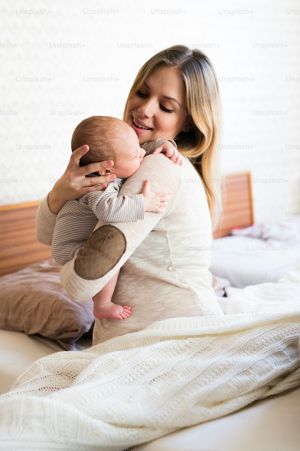 Beautiful young mother holding her baby son in her arms, sitting on bed