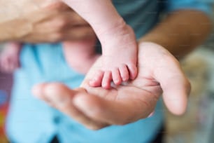 Unrecognizable father with newborn baby son, holding his foot in his hand. Close up.