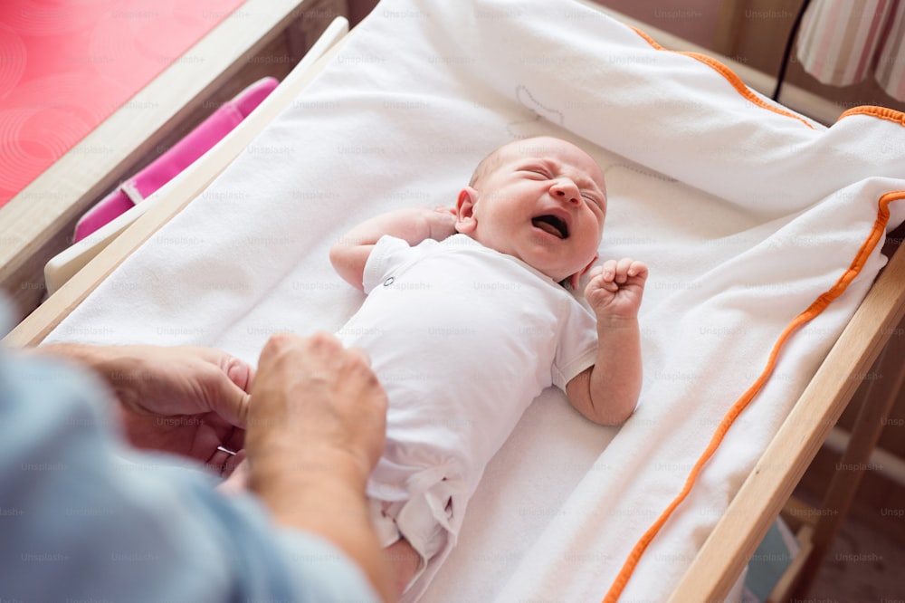 Unrecognizable father changing diaper to his crying baby son lying on nursery table