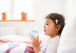 Cute little girl holding bottle with tea at home sitting on sofa in living room