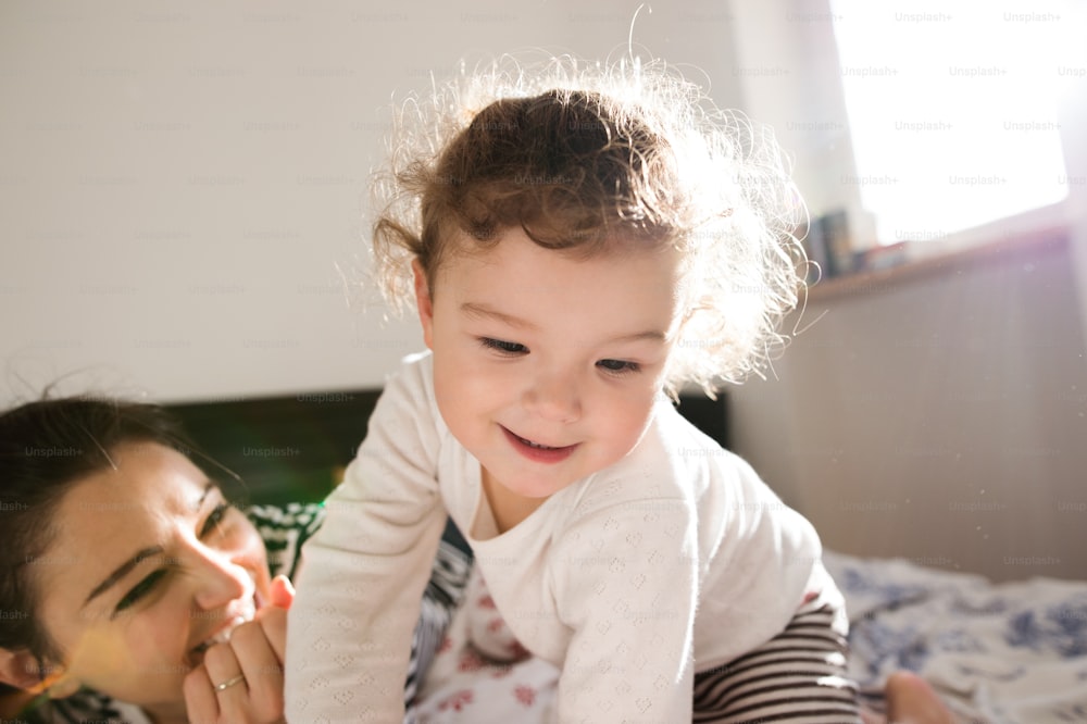 Beautiful young mother with her cute little daughter lying on bed, having fun