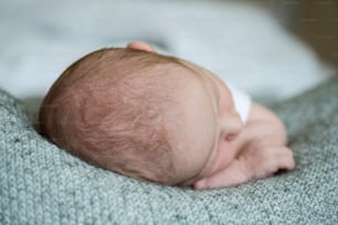 Head of unrecognizable newborn baby boy lying on bed, close up