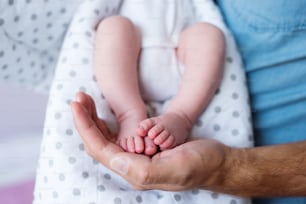 Unrecognizable father with newborn baby son, legs and hand. Close up.