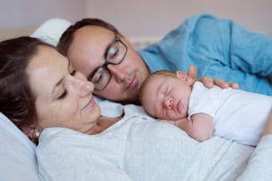 Beautiful young mother and father with their newborn baby son, lying in bed in bedroom