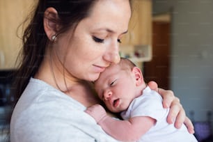 Beautiful young mother in kitchen with her newborn baby son, holding him in her arms. Close up.