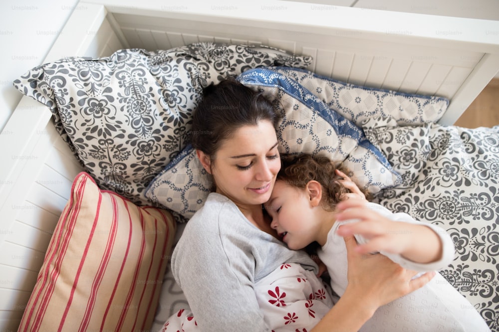 아름다운 젊은 엄마가 침대에 누워 귀여운 딸을 재우고 있다.