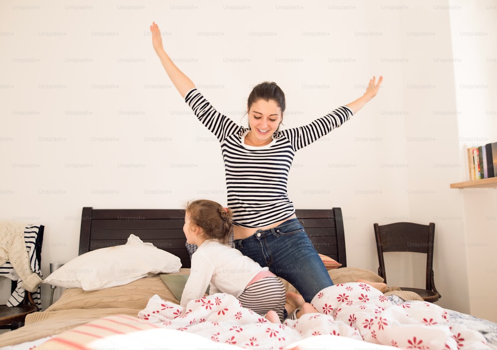 Beautiful young mother having fun with her daughter on bed in her bedroom