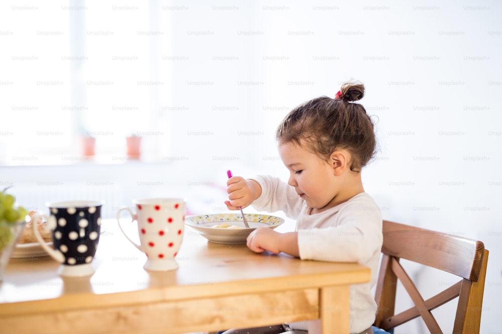 Nettes kleines Mädchen, das am Tisch in der Küche sitzt und frühstückt