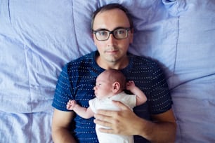 Young father with his newborn baby son, lying in bed in bedroom