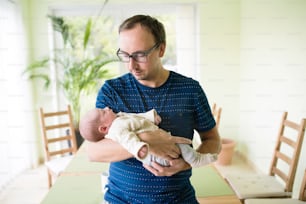 生まれたばかりの赤ん坊の息子を家で腕に抱く若い父親