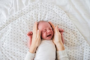 Unrecognizable mother trying to calm down her crying newborn baby son. Close up.