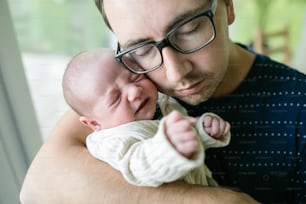 Close up of young father holding his newborn baby son in his arms at home