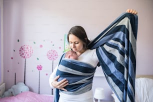 Belle jeune mère enveloppant son nouveau-né dans une écharpe dans sa chambre