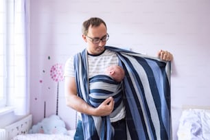 生まれたばかりの赤ん坊の息子を寝室でスリングに包む若い父親