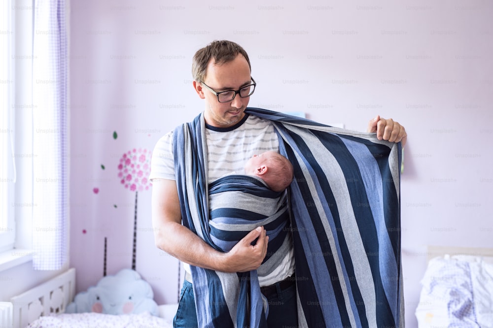 Giovane padre che avvolge il suo figlio neonato in fionda nella sua camera da letto