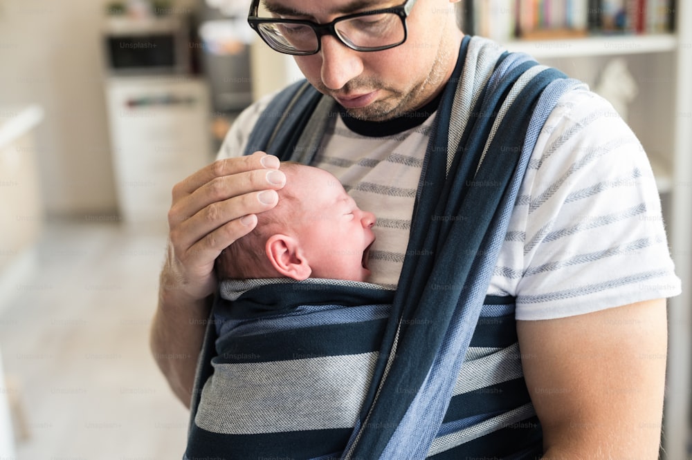 Gros plan d’un jeune père avec son nouveau-né en écharpe à la maison