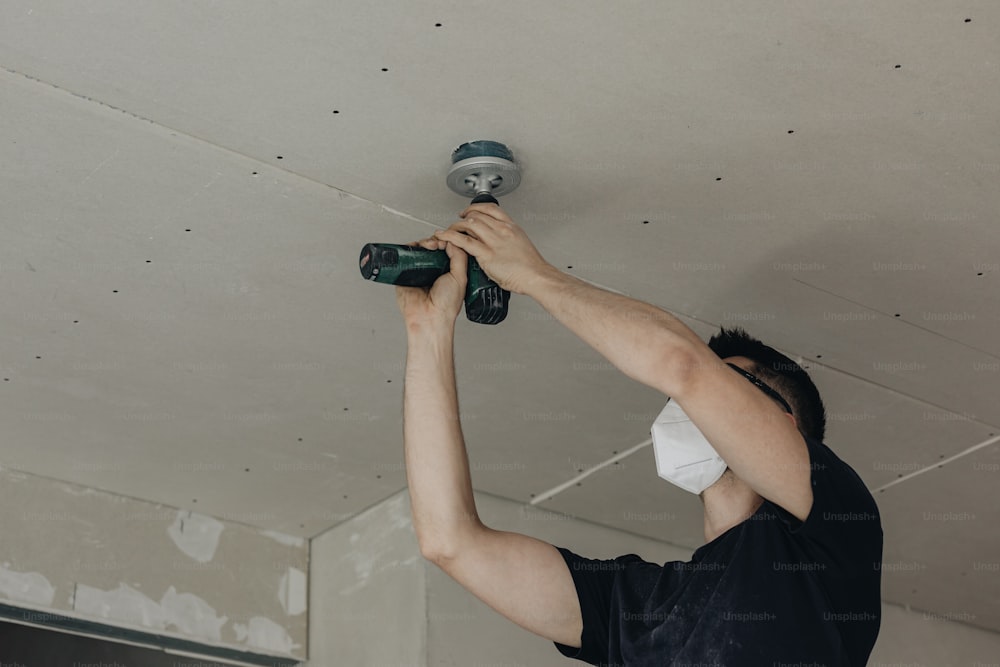 a man in a black shirt and a white mask is fixing a light fixture