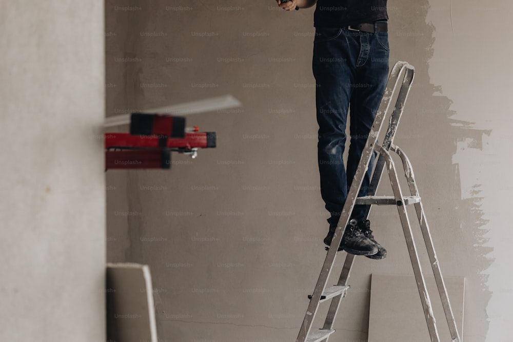 Un uomo in piedi su una scala a pioli che dipinge un muro