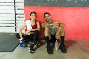 Sporty personal trainers smiling while sitting at the gym and drinking water after their workout session