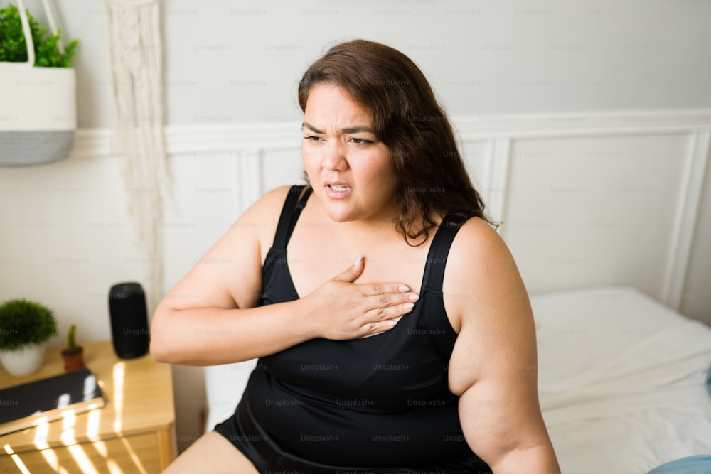 Unhealthy obese woman putting a hand in her chest and having heart problems or suffering from tachycardia