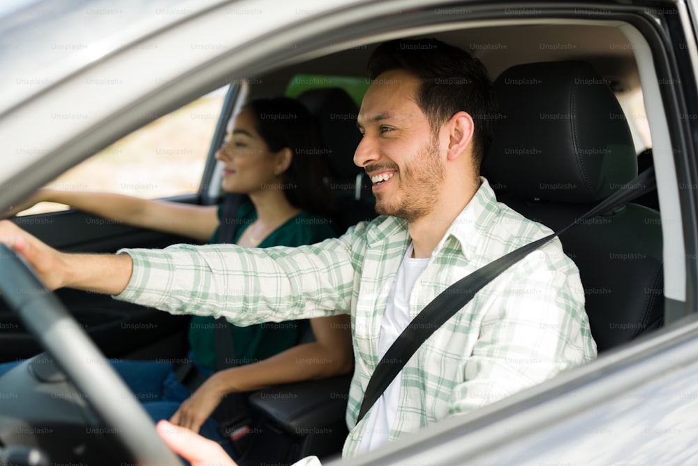 Vista lateral de un alegre hombre latino conduciendo mientras se ríe con su novia durante un divertido viaje en automóvil