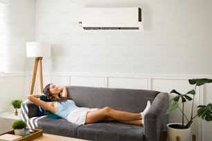 Mulher atraente que relaxa e se sente muito relaxada no sofá enquanto desfruta de sua nova unidade de ar condicionado durante um verão quente
