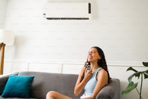 Bella donna che ride nel soggiorno mentre si sente felice per il suo nuovo condizionatore d'aria a casa