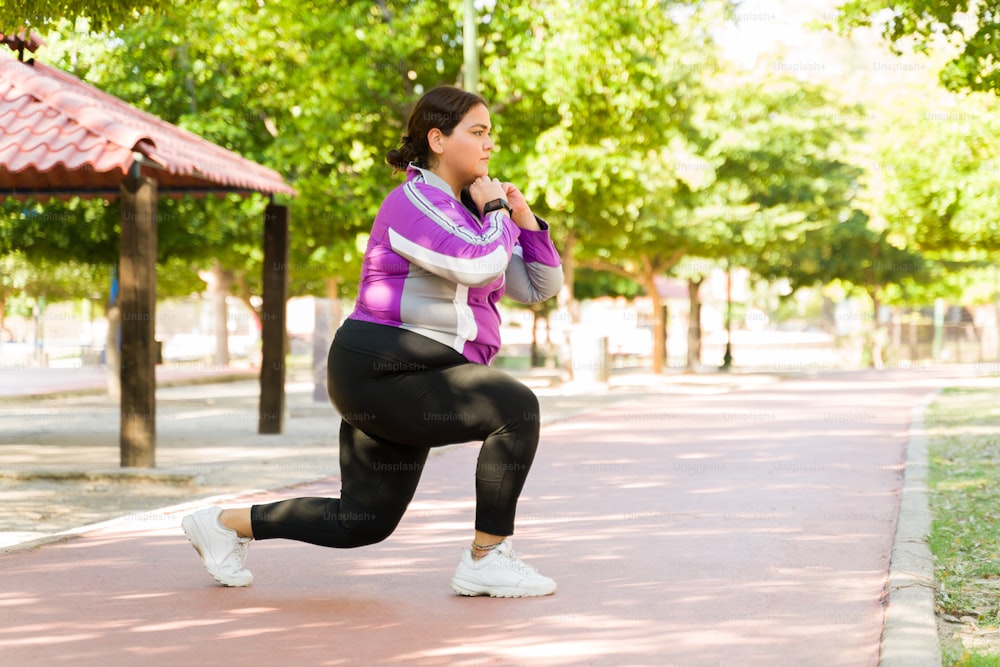 Mujer joven con curvas haciendo estocadas durante su entrenamiento al aire libre. Mujer de talla grande quema calorías para perder grasa corporal y peso
