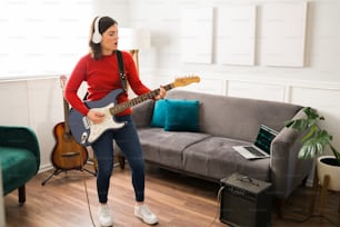 Leidenschaftliche junge Frau, die ein Lied singt, während sie die E-Gitarre spielt, die an einen Verstärker angeschlossen ist