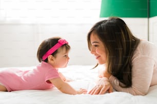 Profile of an adorable baby girl and caucasian young mother smiling while resting in the bedroom