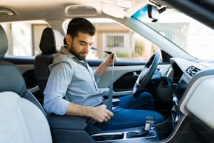 Handsome man putting on the safety seat belt before driving his car to work in the morning