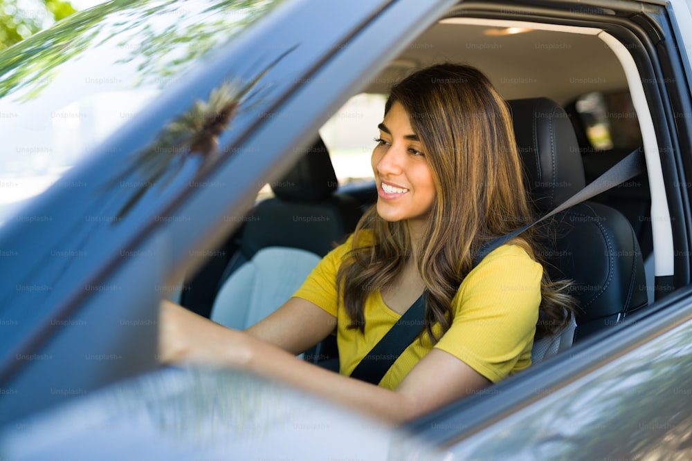 Vista lateral de uma mulher latina com o cinto de segurança em se sentir feliz enquanto dirige seu carro