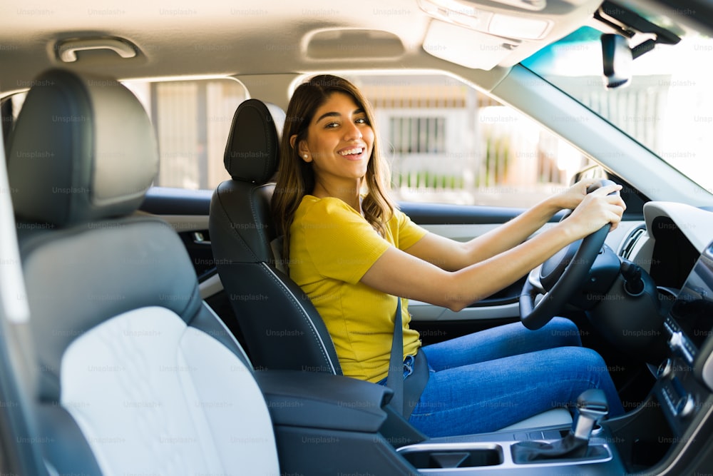Mulher jovem animada fazendo contato visual e sorrindo enquanto dirige para casa seu carro novo