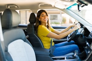 Jeune femme excitée établissant un contact visuel et souriant tout en conduisant sa nouvelle voiture
