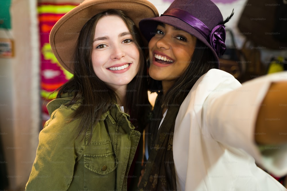 Personal perspective of women best friends shopping and taking a selfie while wearing beautiful hats at the thrift store