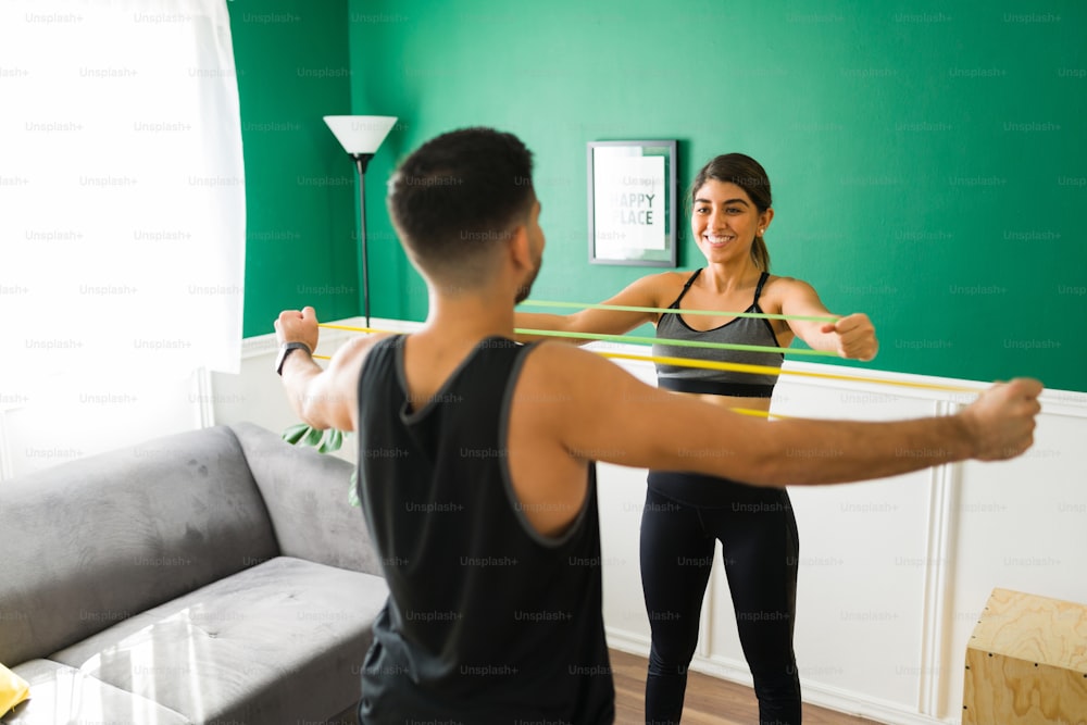 Gorgeous young woman and her workout partner getting stronger arms while working out with resistance bands