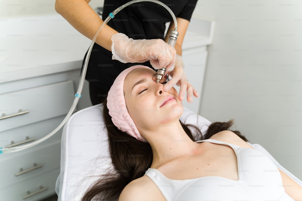 Attraktive junge Frau mit strahlender Haut bekommt eine Mikrodermabrasion mit einer professionellen Kosmetikerin