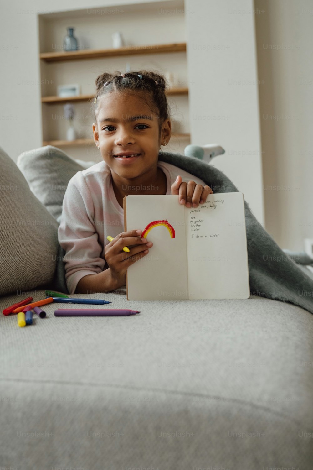 a little girl sitting on a couch holding a piece of paper