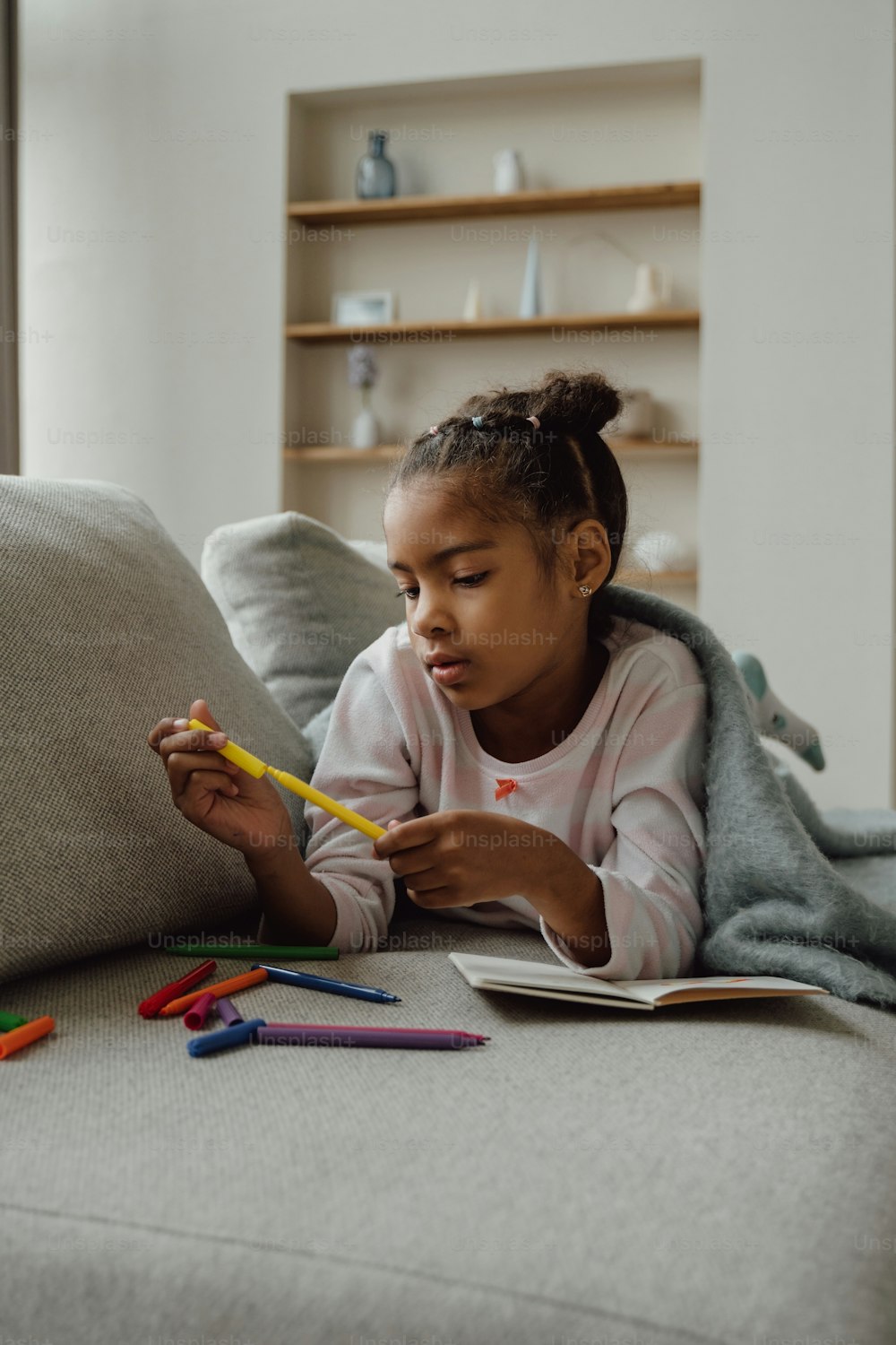 a little girl sitting on a couch with a book and pencils