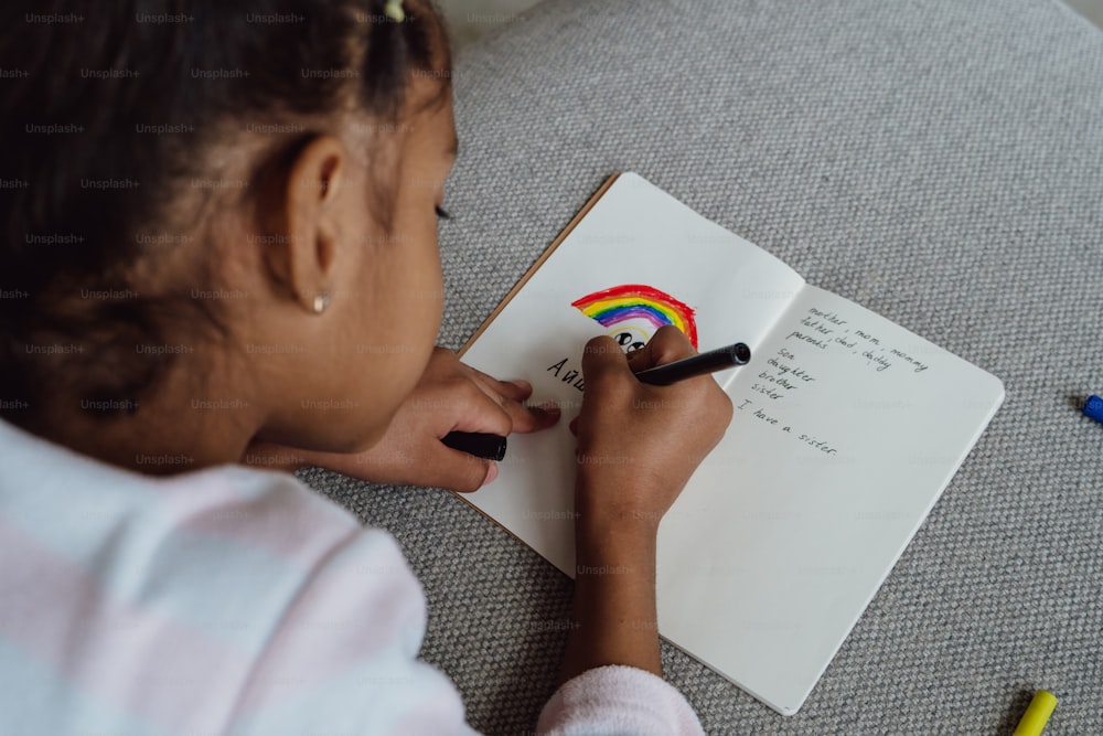 Ein Mädchen, das auf ein Notizbuch schreibt, auf dem ein Regenbogen gezeichnet ist