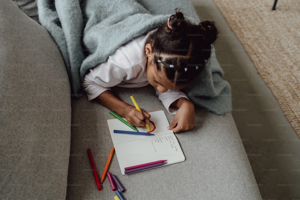 a little girl laying on a couch writing on a piece of paper