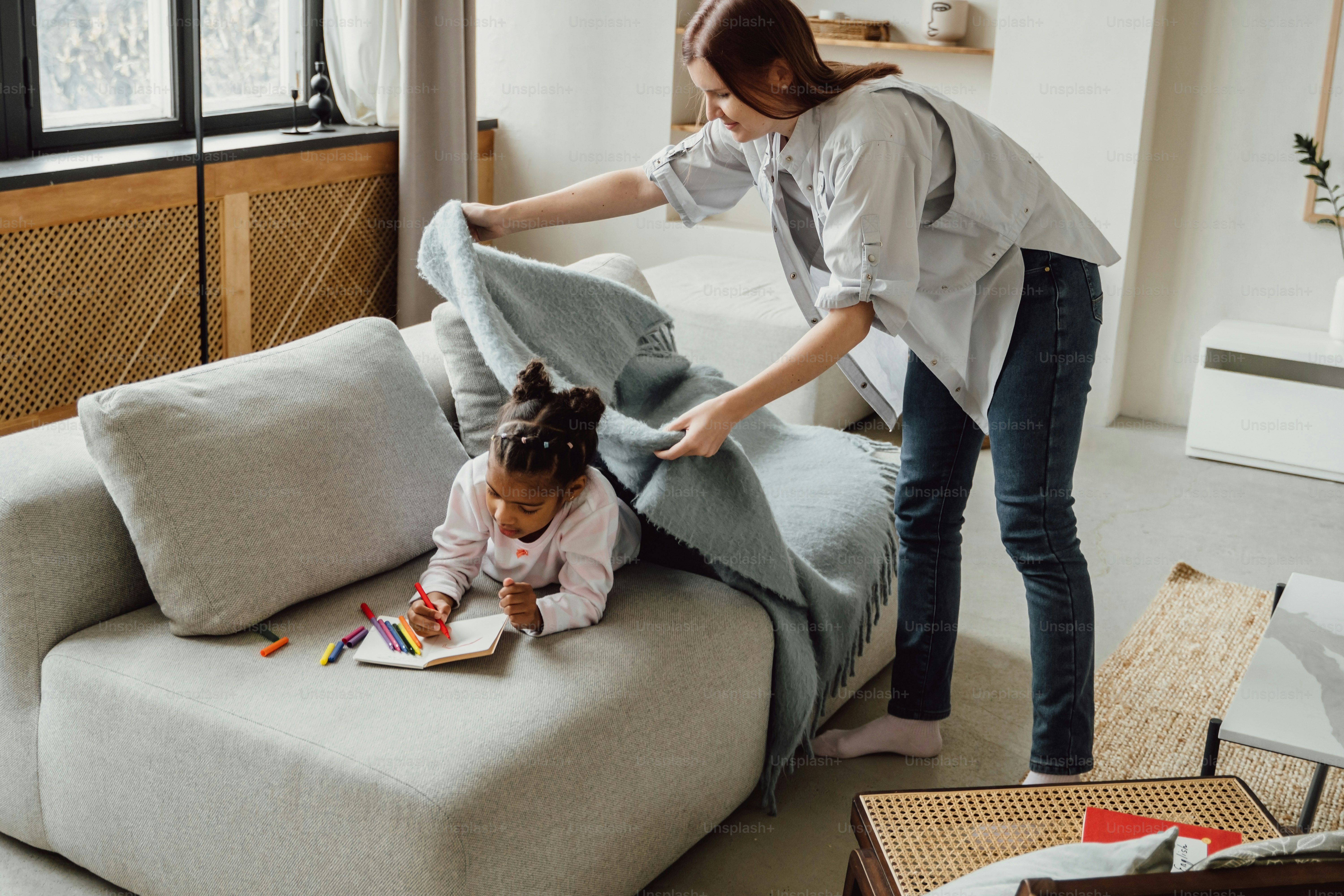 a woman helping a little girl with a book on a couch