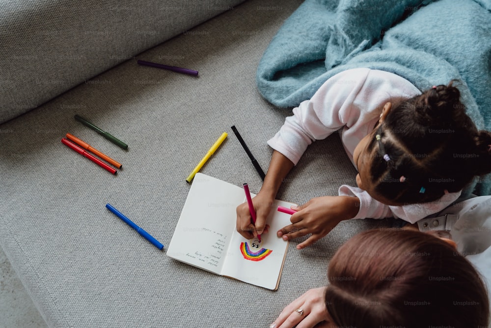 Une petite fille assise par terre dessinant avec des crayons de couleur