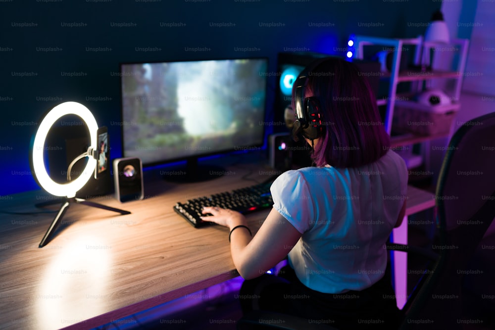 Rear view of a latin female gamer wearing a headset relaxing with a fun action video game on her pc
