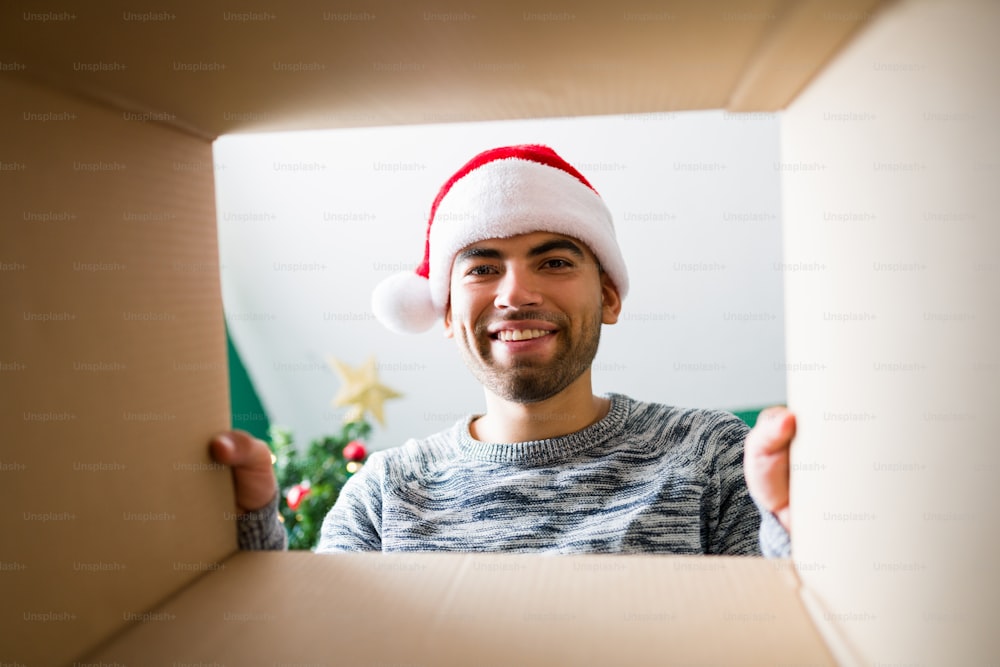 I love christmas gifts. Attractive young man opening a Christmas present and looking inside while smiling