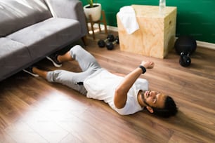 Usar mi reloj inteligente durante un entrenamiento. Deportista latino acostado en el suelo mientras hace ejercicio y mira una aplicación de salud