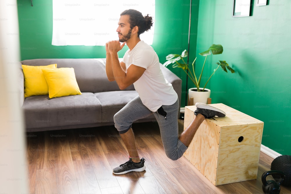 Joven latino en forma haciendo una rutina de entrenamiento cruzado en casa y usando una caja de salto en la sala de estar